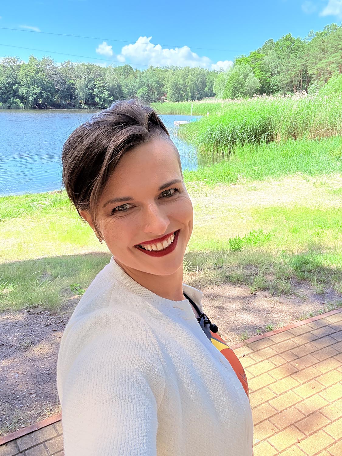 Artystka Karolina robi sobie zdjęcie selfie w słoneczny dzień. Jest uśmiechnięta, stoi w otoczeniu natury.